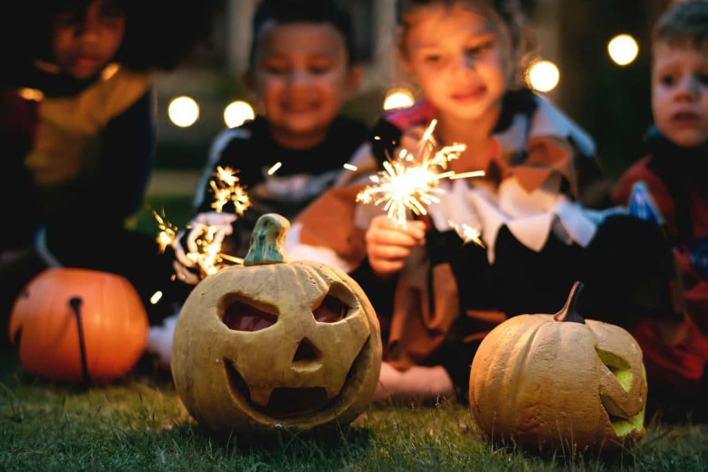 Image of children holding sparklers behind carved out Halloween pumpkins