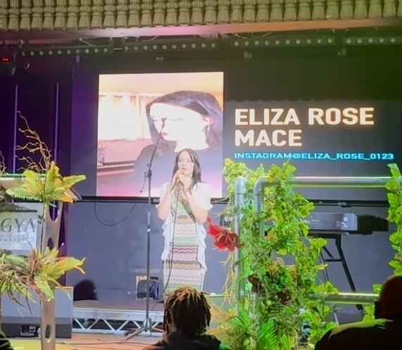 female singer on a stage with lots of greenery in the foreground